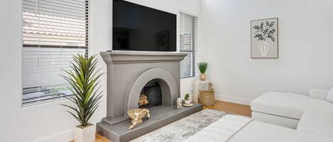 A modern living room with a fireplace, a flat-screen TV, a sofa, and a potted plant.