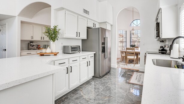 A modern kitchen with white cabinetry, a stainless steel refrigerator, a marble floor, and a dining area with a wooden table and chairs. - Recently Remodeled Avondale Retreat, Private Yard! (Avondale)