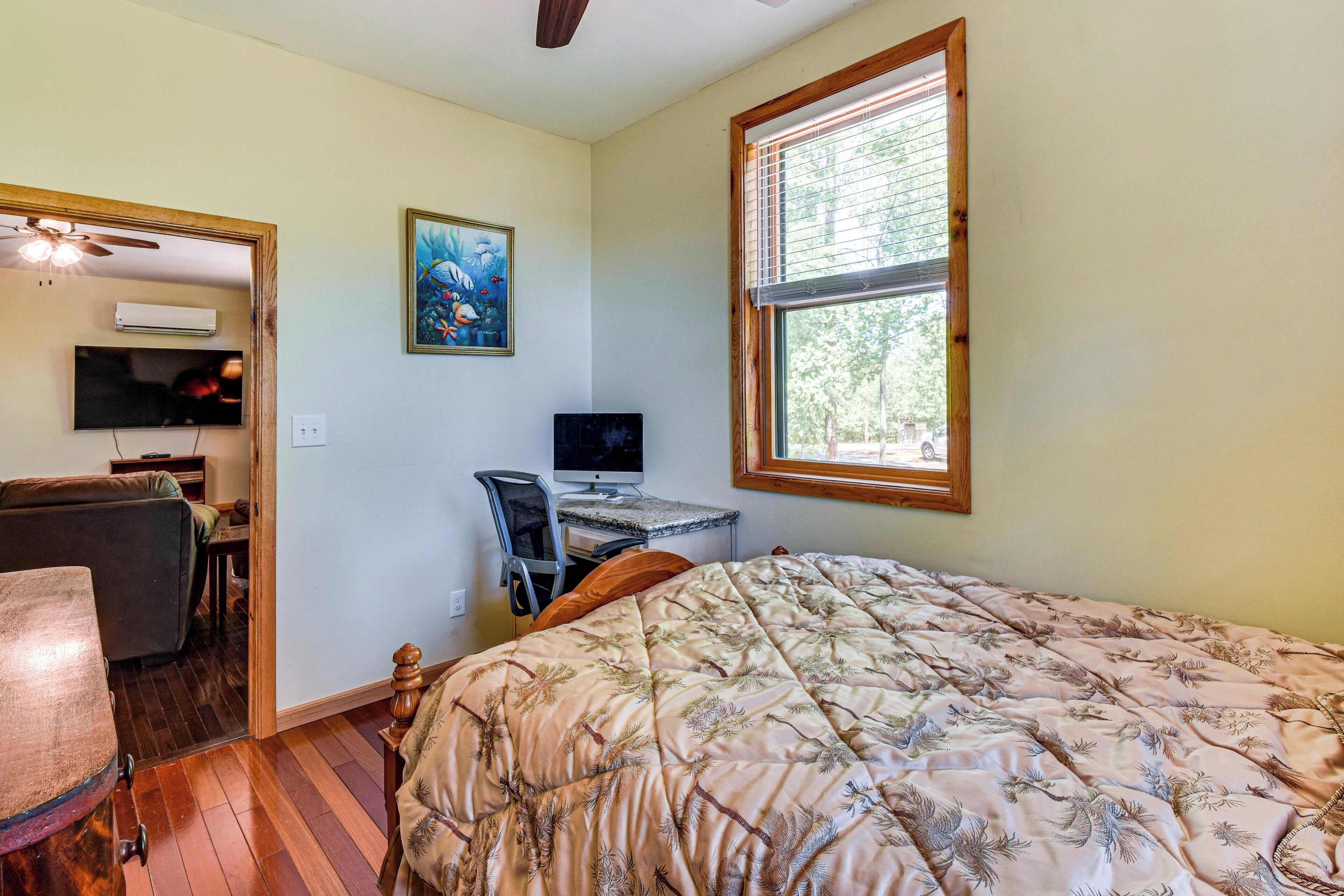 Une chambre à coucher avec un lit, un bureau avec un ordinateur, une chaise, un ventilateur de plafond et une fenêtre.