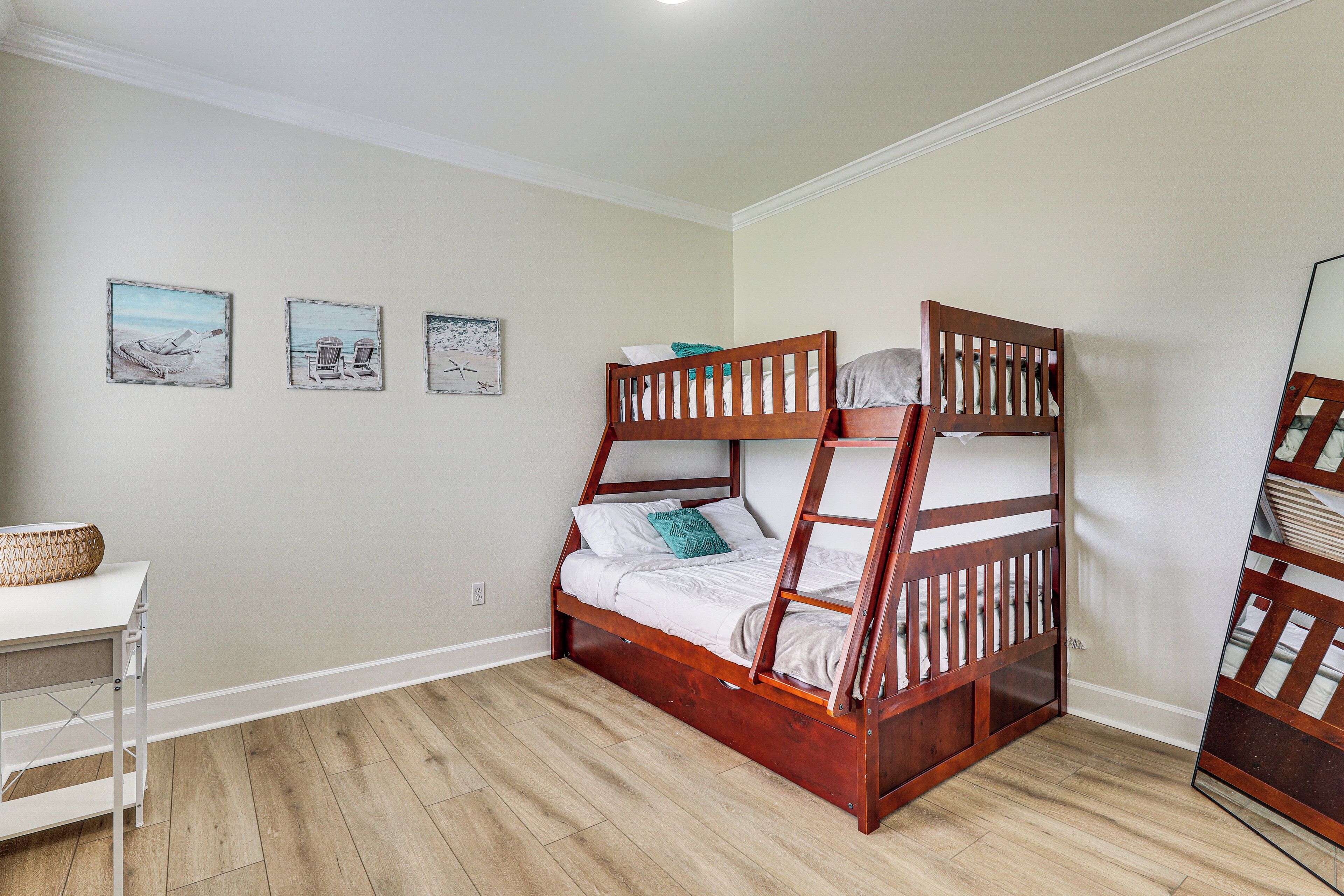 A bunk bed with a wooden frame, a white desk with a basket, and three wall-mounted pictures.