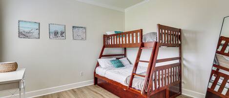 A bunk bed with a wooden frame, a white desk with a basket, and three wall-mounted pictures.