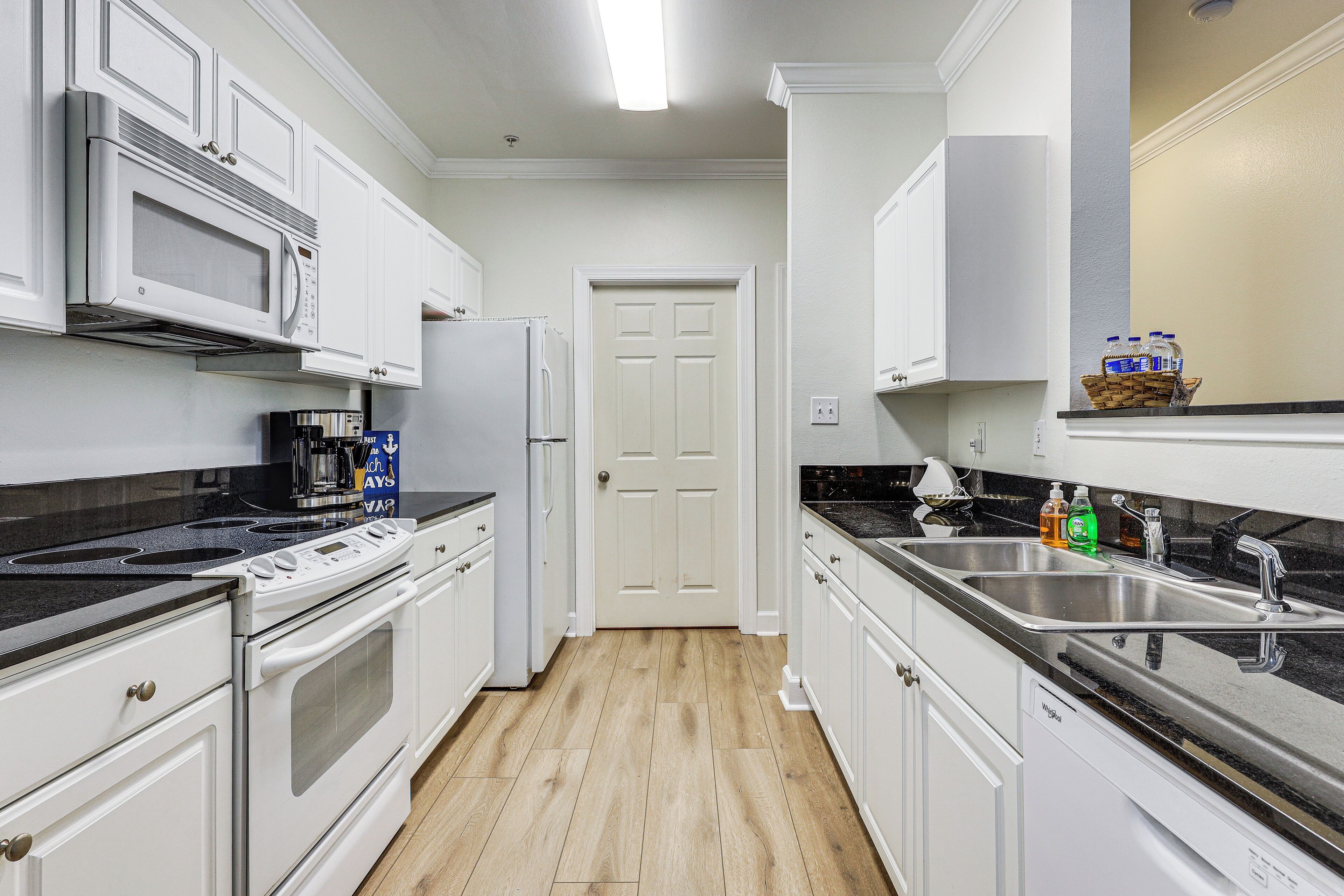 A kitchen with white cabinets, a microwave, stove, and a double sink.