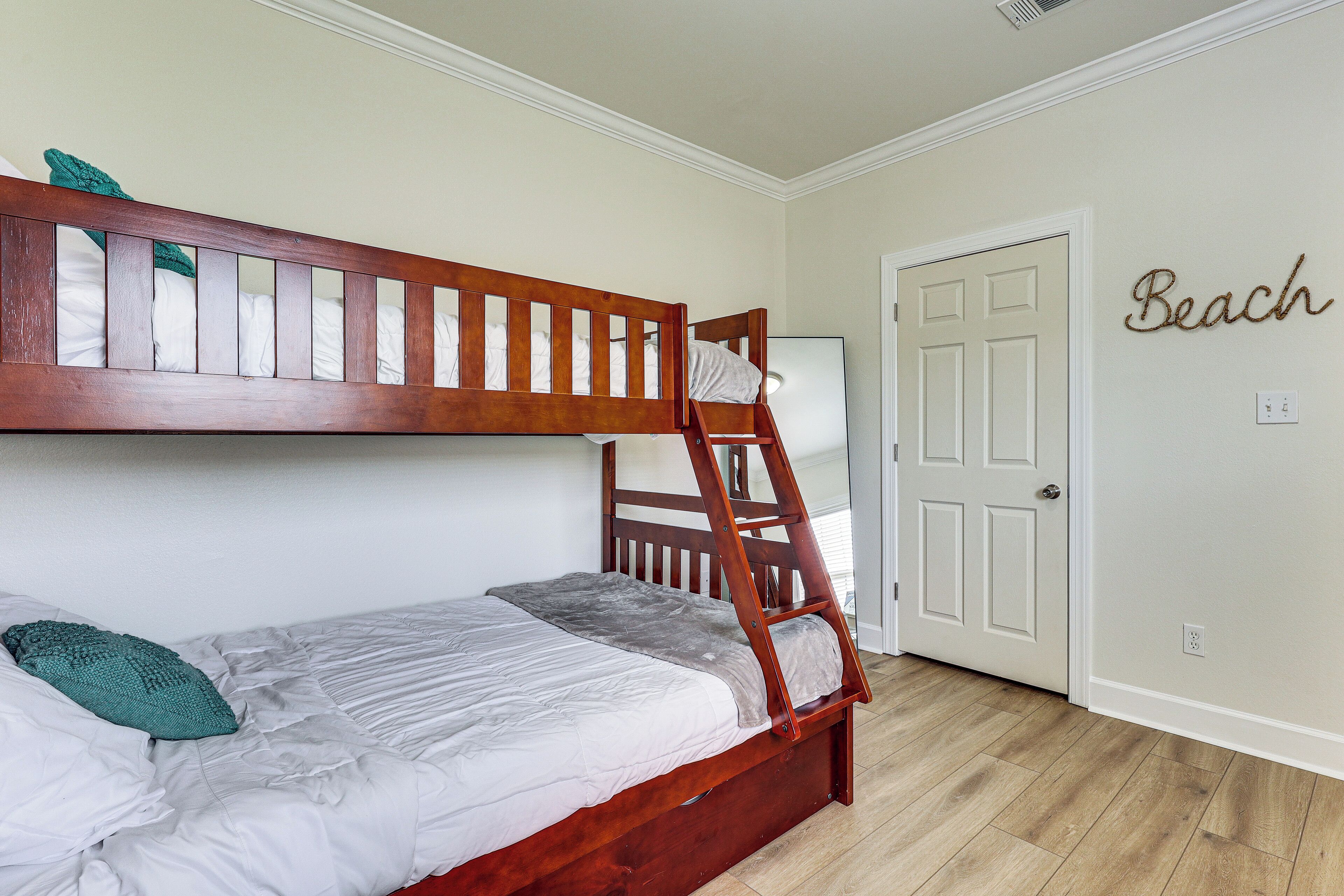 A bunk bed with a ladder, a door with a 'Beach' sign, and a wooden floor.