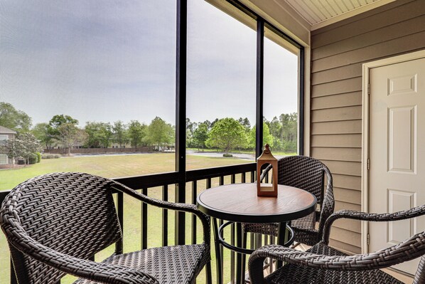 A balcony with wicker chairs, a small round table, and a view of a green landscape. - Pool Access! Recently Updated Coastal Retreat (Foley)