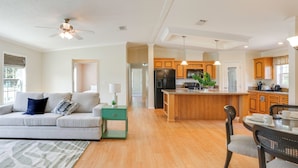 A modern kitchen with wooden cabinets, a central island, and a dining area with a table and chairs. - Pool Access! Spacious Home Near Wekiwa Springs (Apopka)