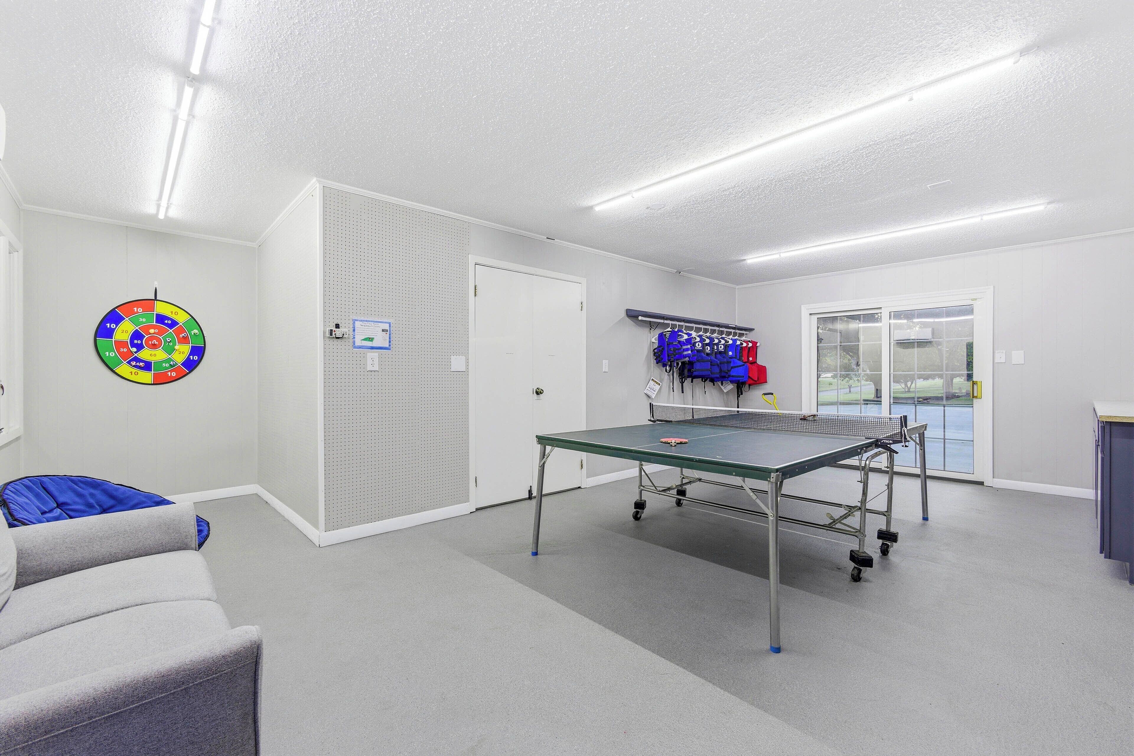 A room with a ping pong table, a dartboard, and a blue chair.