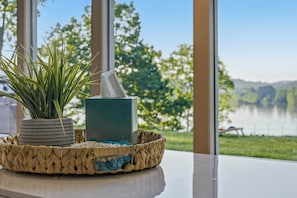 A potted plant, a soap dish, and a woven basket on a table with a view of a lake and trees. - Serenity Dock on Watts Bar Lake- Main Channel View (Harriman)