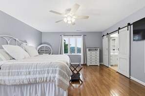 A bedroom with a bed, a ceiling fan, a window with curtains, a dresser, and a TV mounted on the wall. - Serenity Dock on Watts Bar Lake- Main Channel View (Harriman)