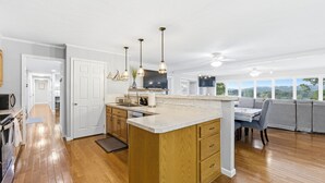 Cocina con una isla de madera, luces colgantes y vistas amplias a través de grandes ventanales.