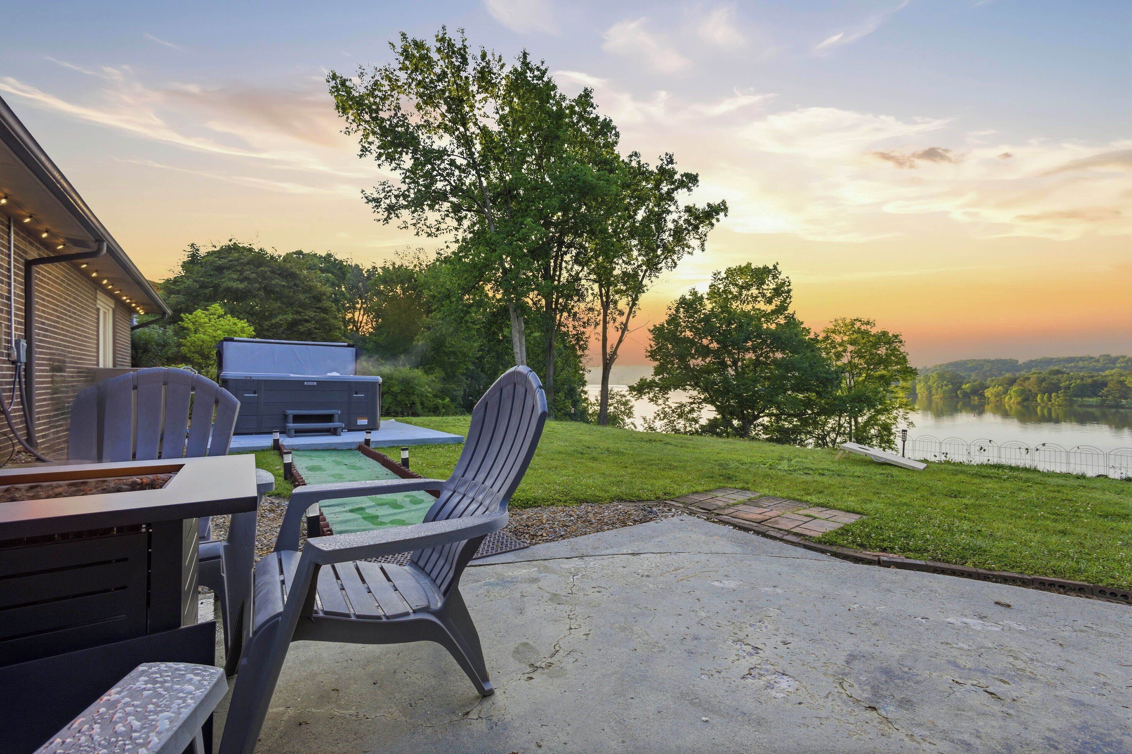Une terrasse extérieure avec un barbecue, des chaises et une vue sur un lac au coucher du soleil.