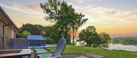 Une terrasse extérieure avec un barbecue, des chaises et une vue sur un lac au coucher du soleil.