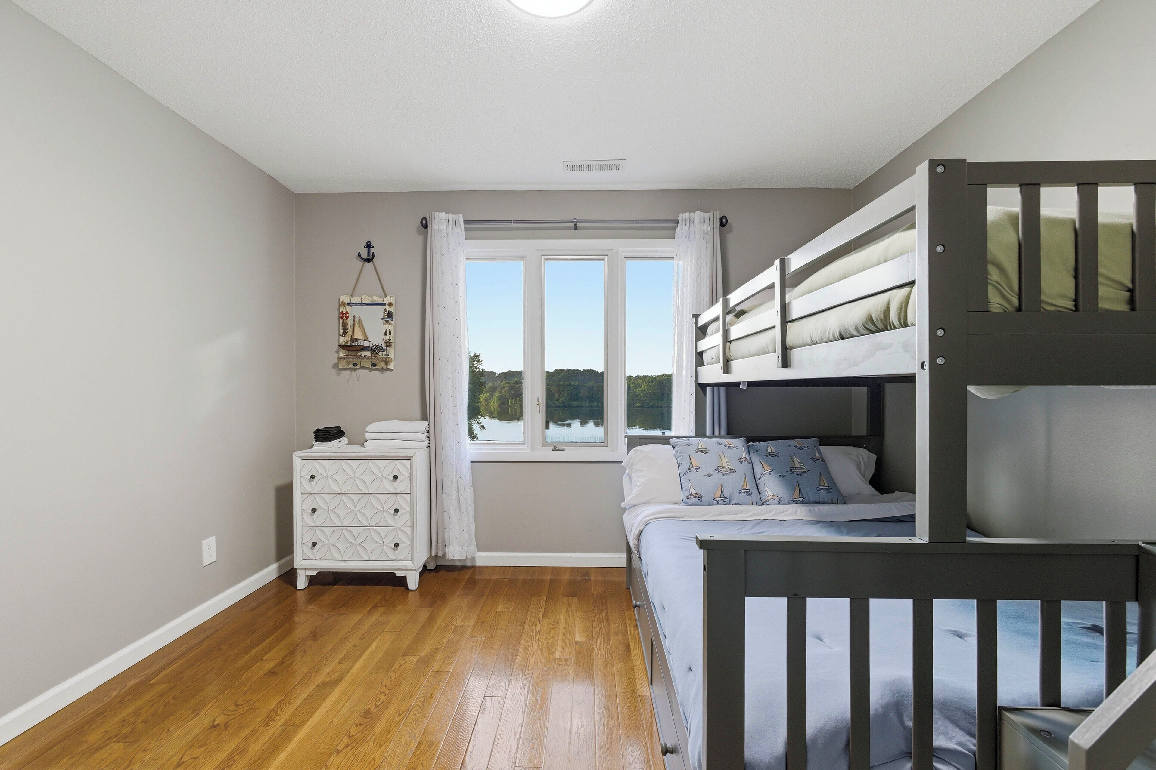 A bedroom with a bunk bed, a dresser, a window with curtains, and a view of the outdoors.