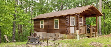 A log cabin with a porch, a fire pit, and a chair.