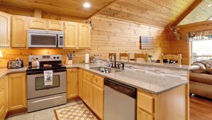 Ein Interieur einer Holzhütte mit einer Küche, die Holzschränke, eine Mikrowelle, einen Herd und einen Geschirrspüler zeigt.