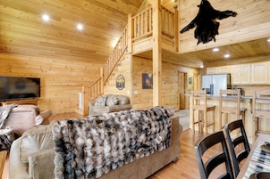 Interior de una cabaña de troncos con sala de estar, cocina y una escalera.