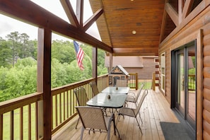 A wooden deck with a table and chairs, an American flag, and a view of trees.