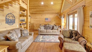 Ein gemütliches Blockhaus-Interieur mit Holzwänden, einer Couch, einem Zweisitzer und einem Essbereich.