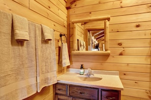 Baño de cabaña de madera con lavamanos, espejo y toallas.
