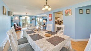 A dining area with a table set for four, white chairs, a chandelier, and a kitchen in the background. - Walk to the Beach! Boyne City Escape w/ Lake Views (Boyne City)