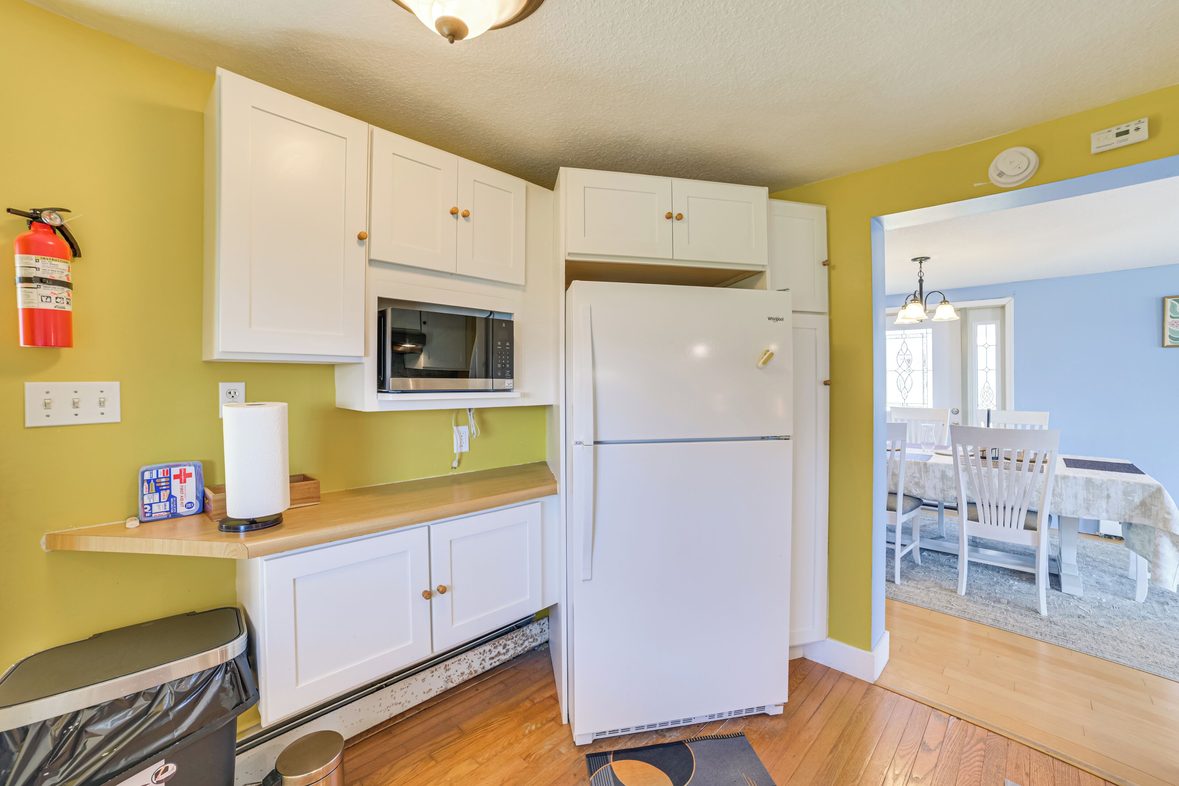 A compact kitchen with white cabinets, a microwave, a refrigerator, and a fire extinguisher on the wall.