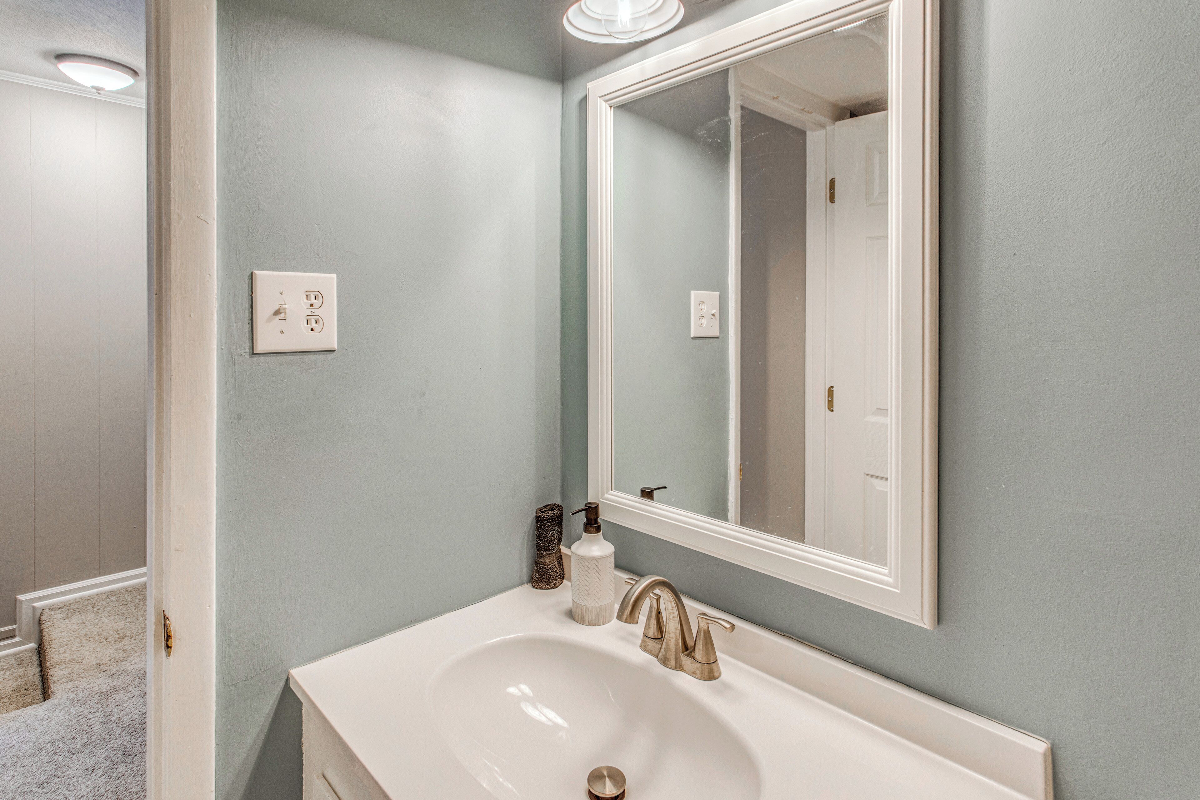 A bathroom with a white sink, a mirror, and a light switch on the wall.