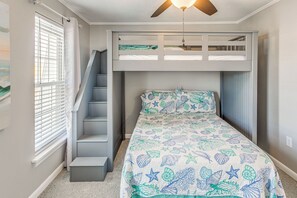 Ein Schlafzimmer mit Etagenbett, Treppe, Deckenventilator und Fenster mit Jalousien.