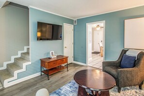 Ein Wohnzimmer mit Treppe, Flachbildfernseher, Couchtisch aus Holz und bequemen Sesseln.