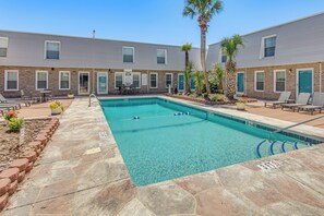 A rectangular pool with clear blue water, surrounded by a stone deck, and adjacent to a building with brick and siding exteriors. - Walk to Ocean! Family Haven in North Myrtle Beach (North Myrtle Beach)