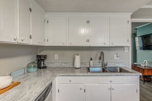 A kitchen with white cabinets, a marble countertop, a coffee maker, a roll of paper towels, and a sink. - Walk to Ocean! Family Haven in North Myrtle Beach (North Myrtle Beach)
