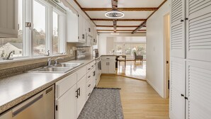 Una cocina con armarios blancos, encimera de granito, lavavajillas y ventana con vistas a casas.