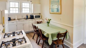 Une cuisine avec des meubles blancs, une cuisinière à gaz, un four à micro-ondes et une table à manger avec des chaises.