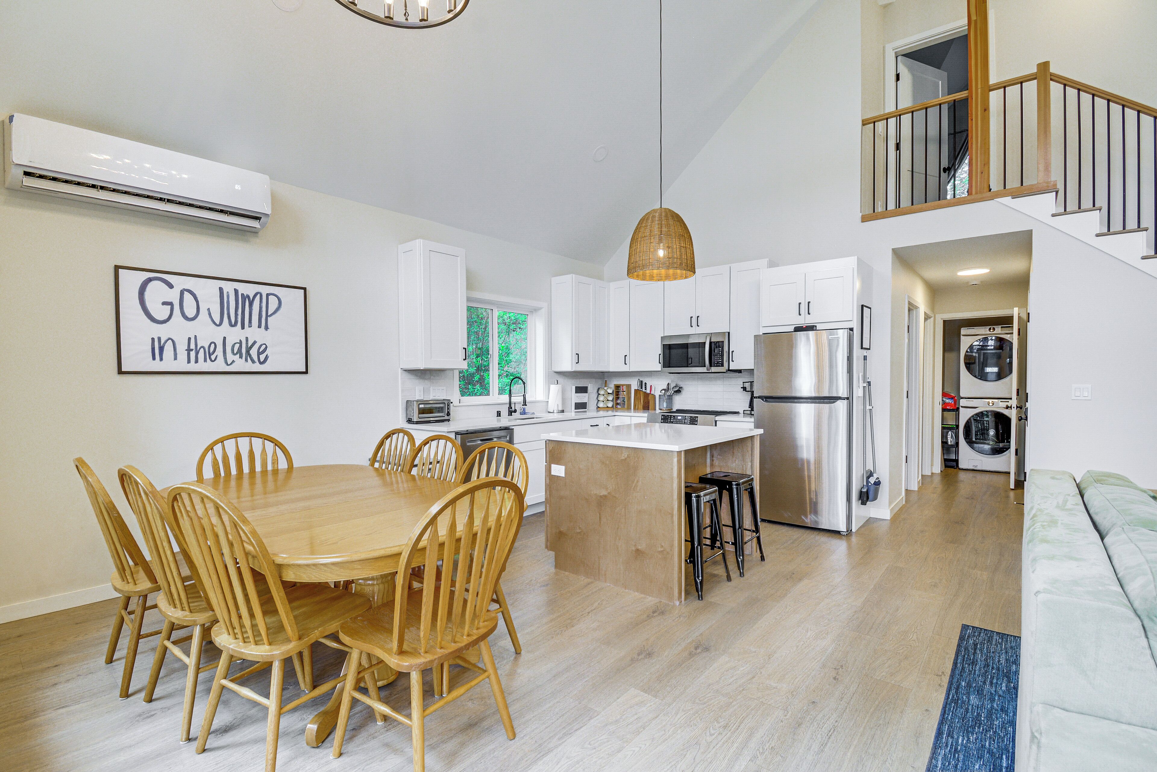 Una cocina moderna con armarios blancos, una isla central y un comedor con sillas de madera.
