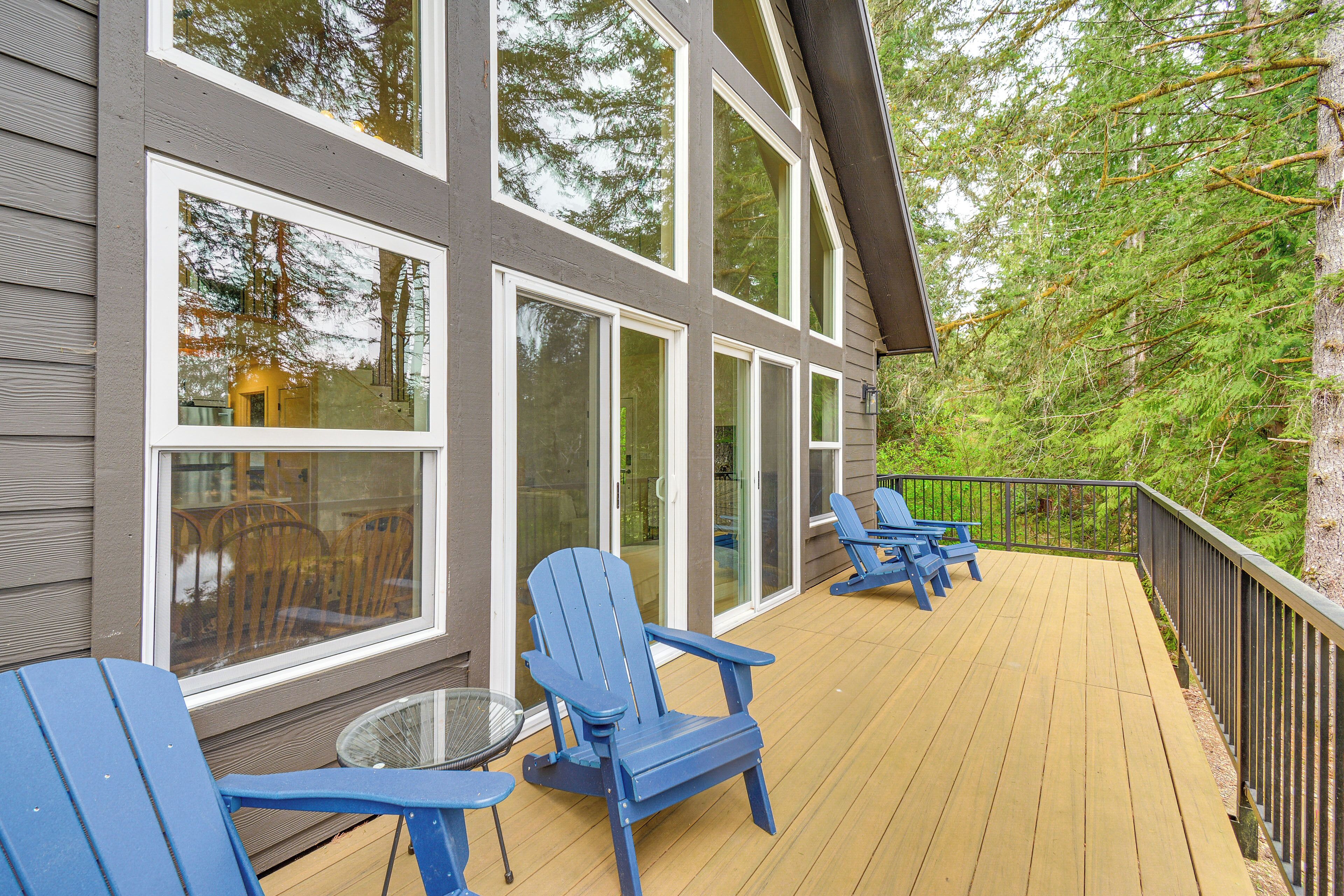 A deck with blue Adirondack chairs, a small table, and a glass door leading to a covered area.
