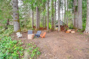 A forested area with a cabin, outdoor seating, and a dirt ground. - Lakeside Bliss in Tahuya! Modern Family Getaway (Tahuya)