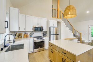 Eine moderne Küche mit weißen Schränken, Edelstahlgeräten, einer Holztreppe und einer Hängeleuchte.