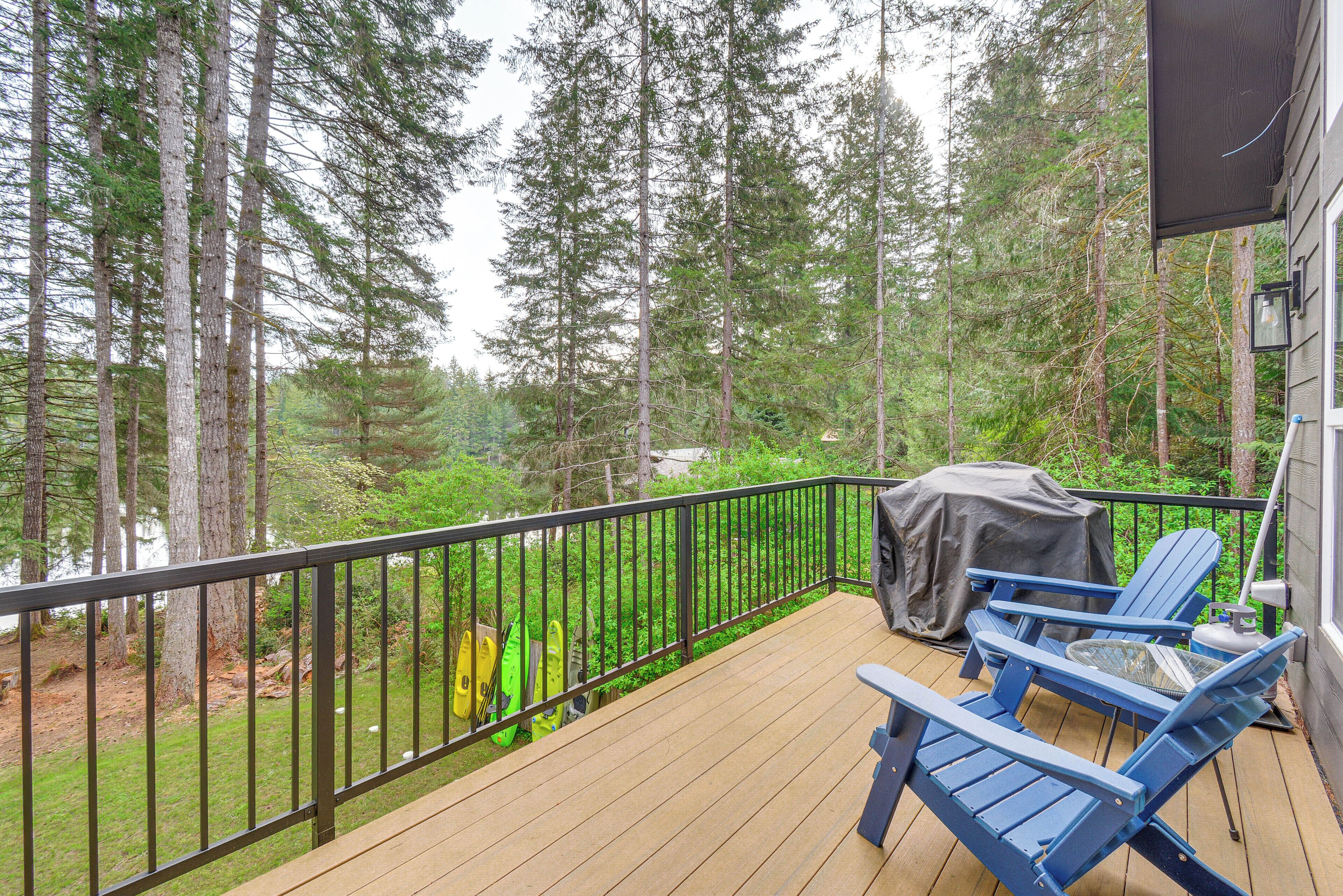 A deck with a black railing, two blue Adirondack chairs, and a grill.