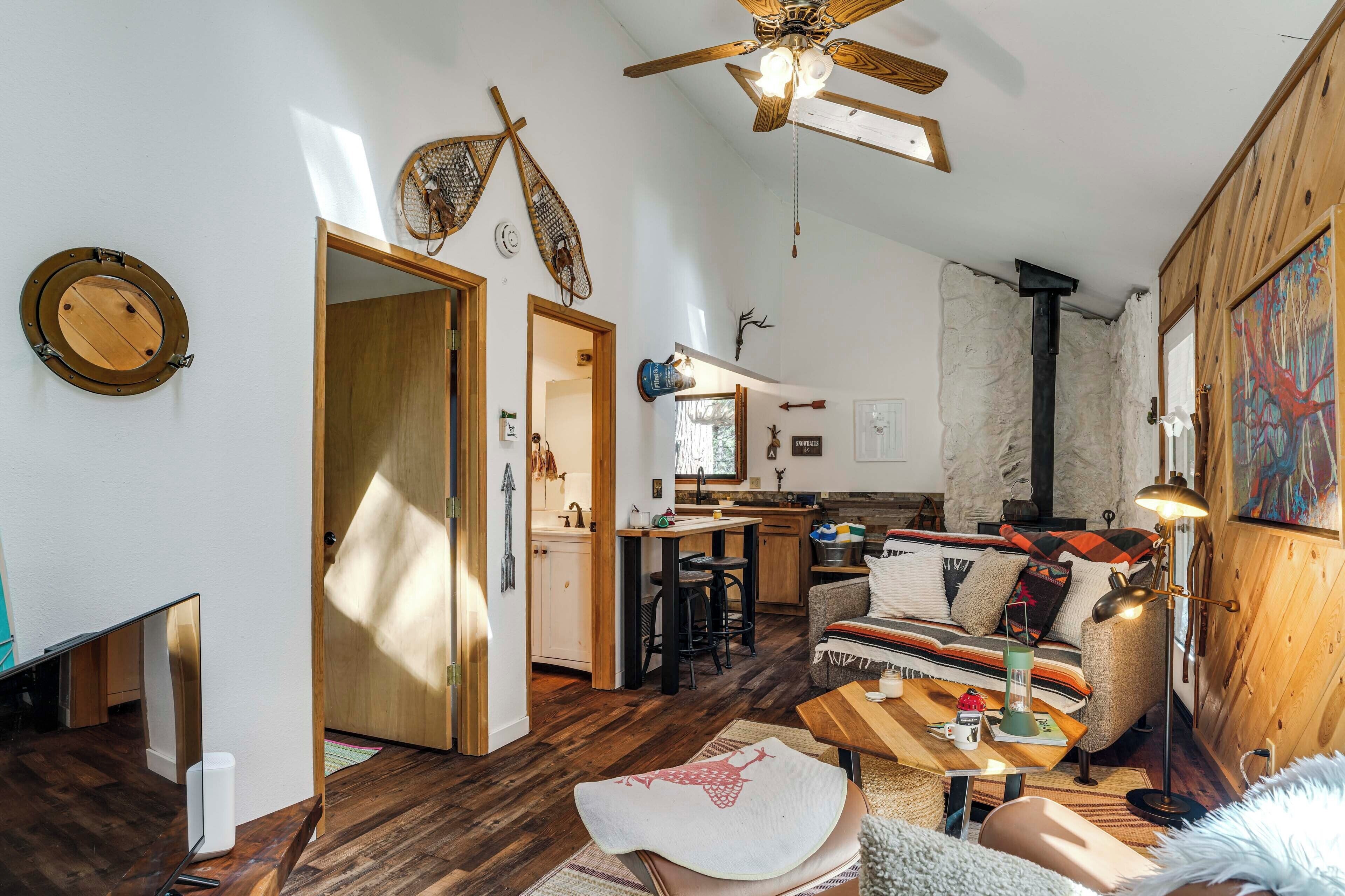 A cozy living room with a wooden ceiling fan, a dining area with a table and chairs, and a kitchen in the background.