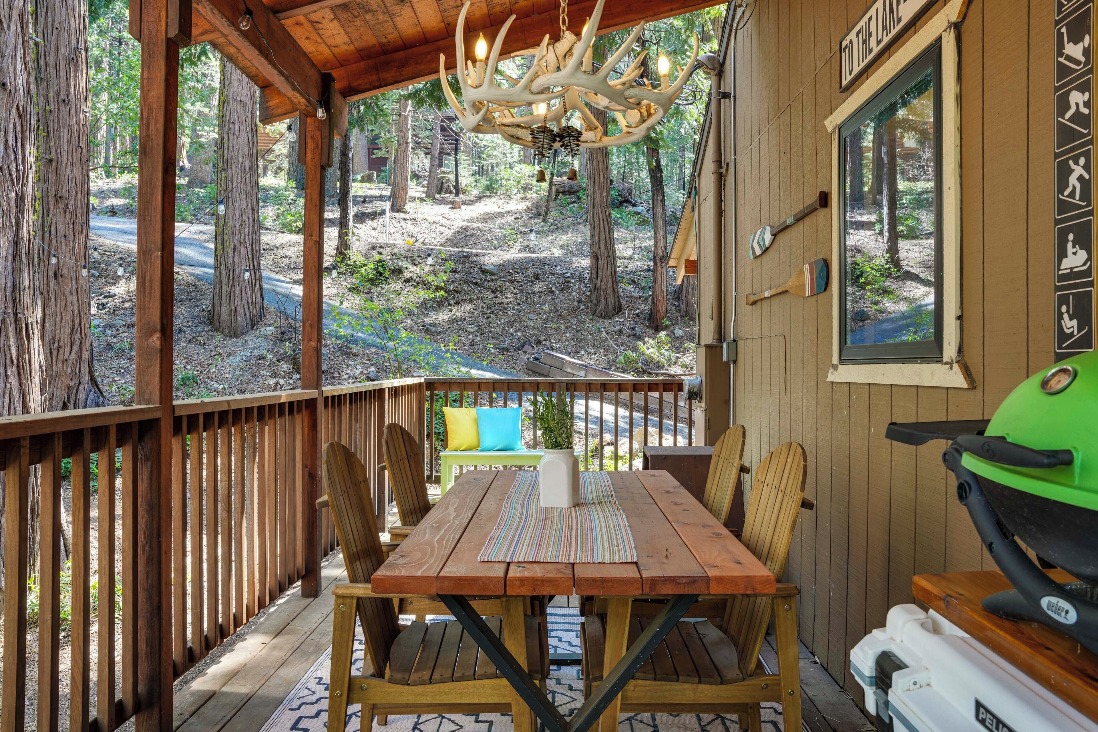 A wooden deck with a table and chairs, a grill, and a view of the forest.