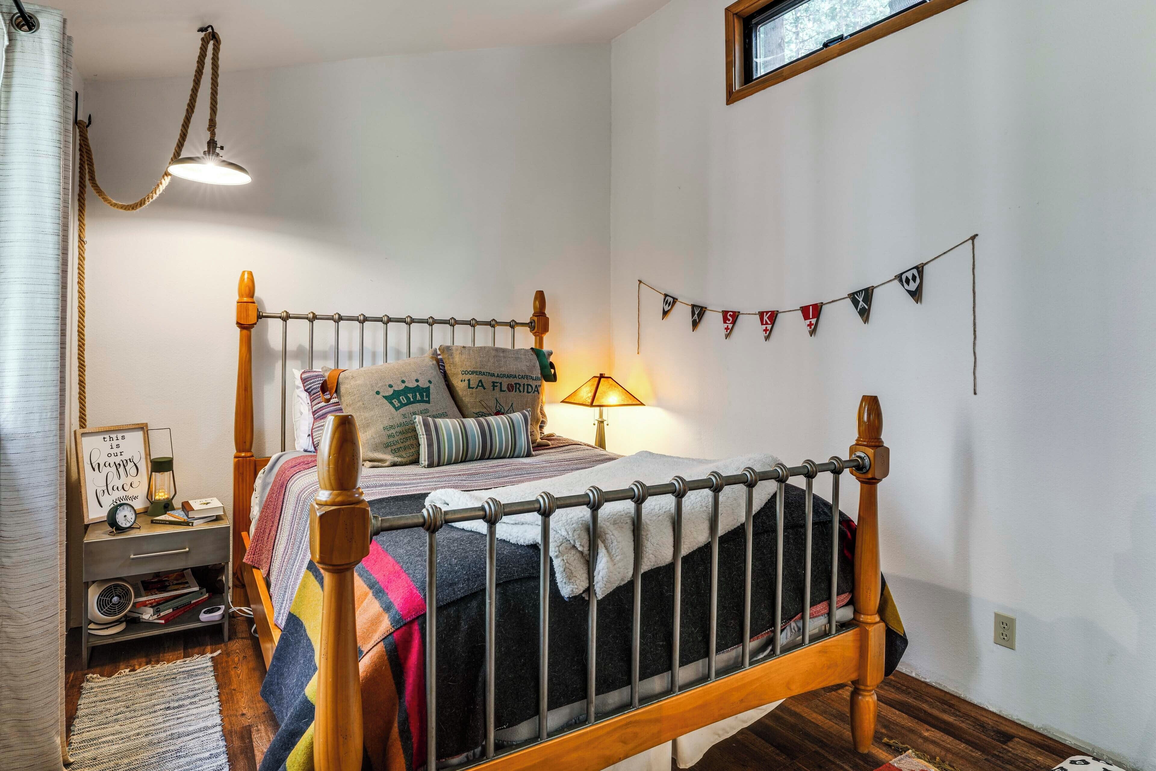 A bedroom with a wooden bed, a nightstand with a lamp, a wall clock, and a window with a view.