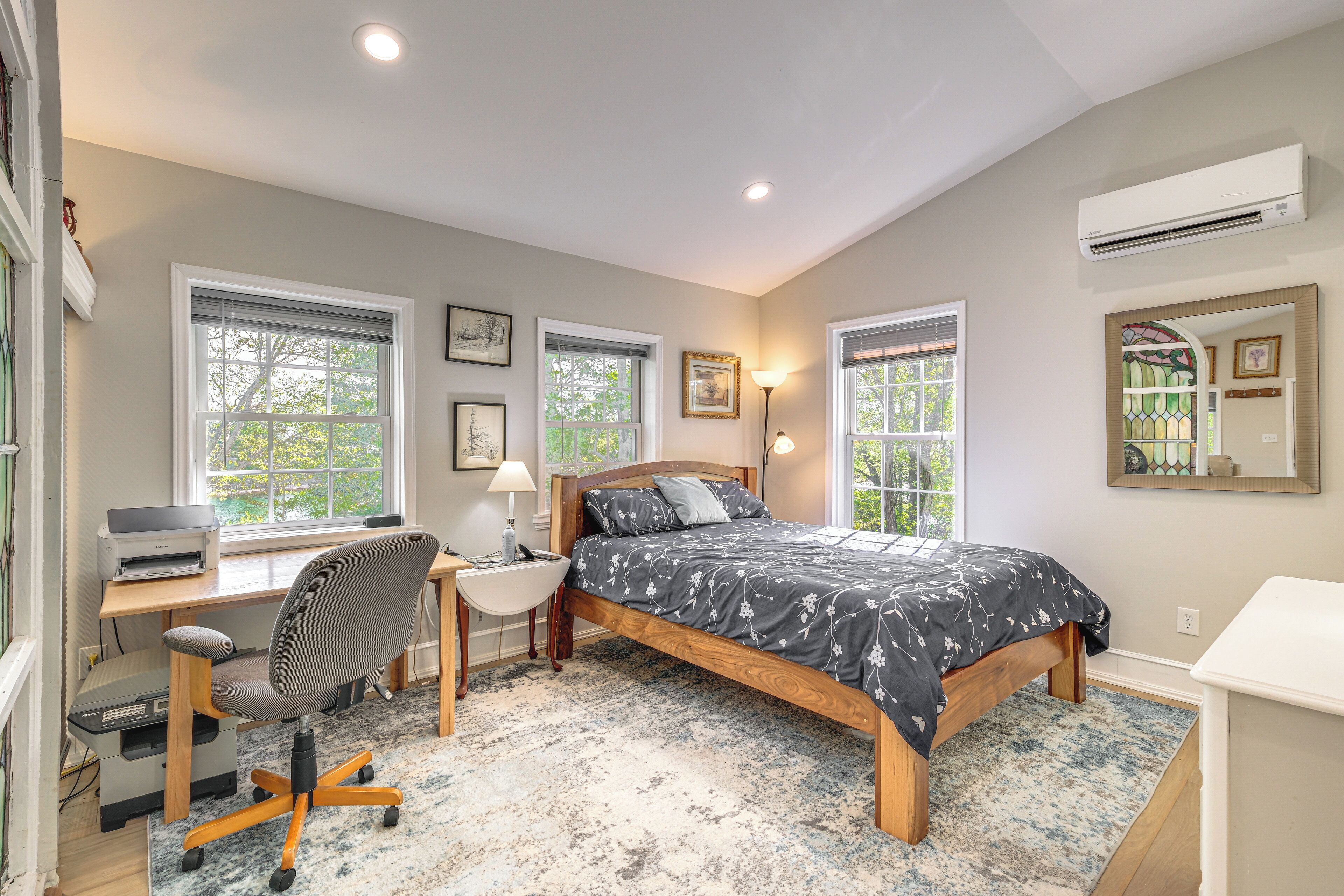 A bedroom with a bed, desk, chair, and a large window.