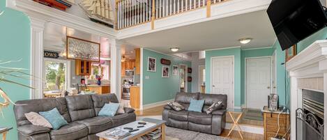 A spacious living room with a high ceiling, a fireplace, and a balcony with a railing.