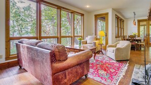 A spacious living room with large windows, a red patterned rug, and a leather sofa.
