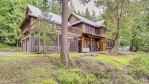 A large wooden cabin with multiple windows and a porch, surrounded by dense forest.