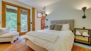 A bedroom with a large bed, a chair, a nightstand, and a view through a glass door.
