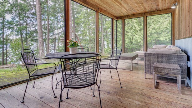 A covered outdoor area with a wooden ceiling, large windows, and a dining table with chairs.