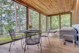 Un espacio al aire libre techado, con techo de madera, ventanas amplias y una mesa de comedor con sillas.