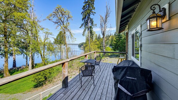 A wooden deck with outdoor furniture, a railing, and a view of a lake. - Private Beach & Hot Tub! Family Gem on Puget Sound (Shelton)