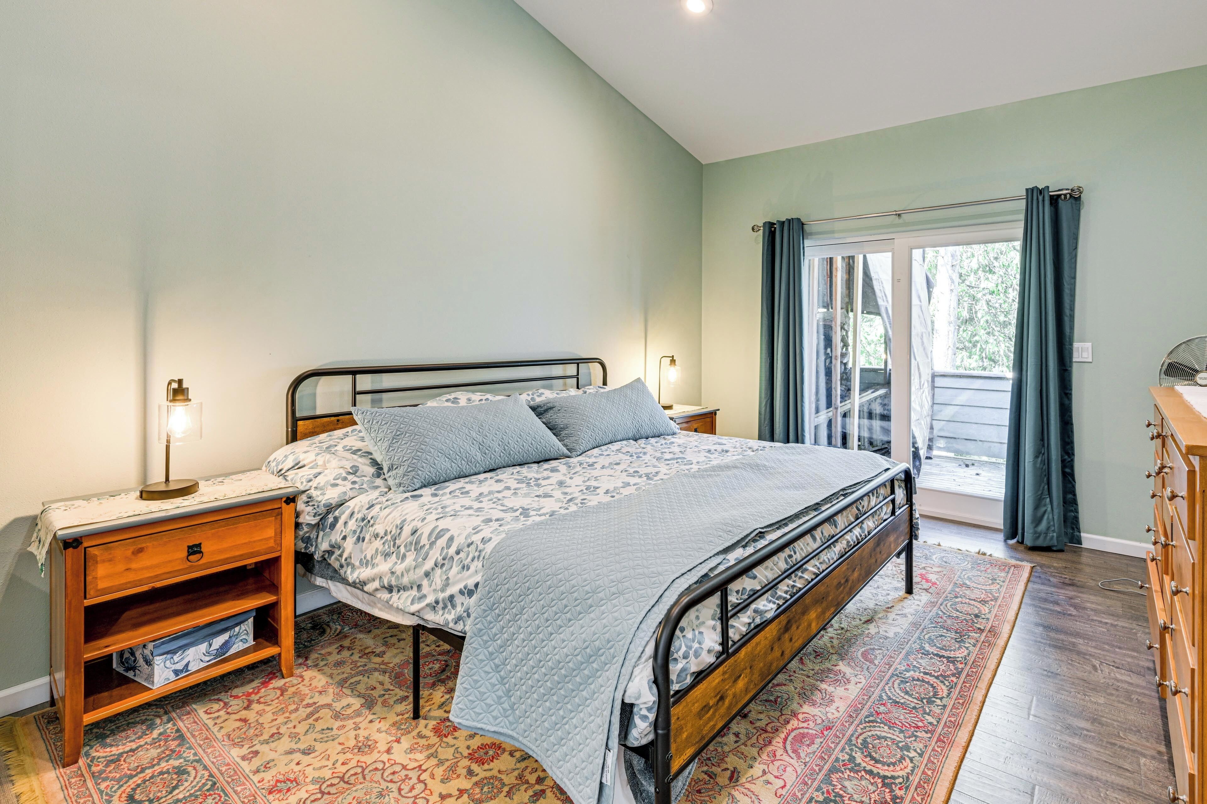 A bedroom with a bed, bedside table, lamp, and a view of the outdoors through a sliding door.