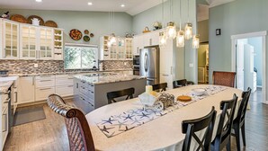 A modern kitchen with white cabinetry, a central island, and pendant lighting. - Private Beach & Hot Tub! Family Gem on Puget Sound (Shelton)