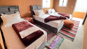 Habitación de hotel con tres camas, un colorido tapiz a rayas y vistas al exterior a través de las ventanas.